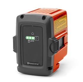 Akumulator Husqvarna BLi20 w kolorze czarnym z pomarańczowymi elementami. Widoczny wskaźnik naładowania z diodami LED. Produkt stoi w pozycji leżącej, z widocznym logo Husqvarna oraz etykietą z informacjami technicznymi. Tło białe.