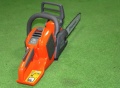 Pilarka akumulatorowa Husqvarna 535i XP w kolorze pomarańczowym z szarym uchwytem, w pozycji stojącej, widoczna z boku. Na obudowie widoczne przyciski sterujące i etykiety ostrzegawcze. Wydłużony łańcuch i metalowy prowadnik wyraźnie eksponowane.