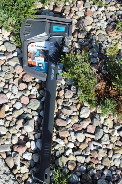 Siekiera rozłupująca GARDENA 2800S, z ergonomicznie uformowaną rączką, w kolorze czarnym. Widoczna głowica z logo na tle kamieni. Produkt leży na ziemi w ogrodzie, z widoczną etykietą i złączem na uchwycie.