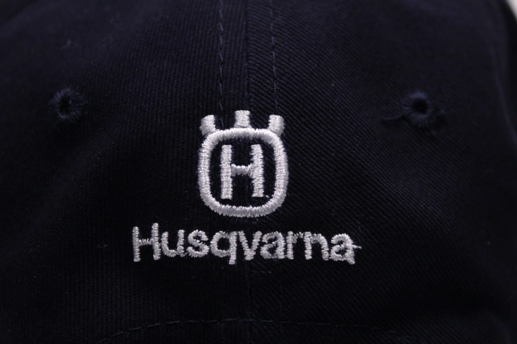 Granatowa czapka z daszkiem Husqvarna z białym haftem logo. Ujęcie zbliżeniowe na tył czapki, ukazujące wyraźne napisy oraz fakturę materiału. Czapka ma charakterystyczny kształt z daszkiem, wykonana z trwałego materiału.