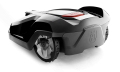 Automower® 440 to robot koszący w kolorze czarno-szarym, z wyraźnym logo Husqvarna. Ujęcie z boku ukazuje zaokrąglony kształt i duże koła. W górnej części widoczny jest czerwony przycisk, co wskazuje na funkcję uruchamiania.