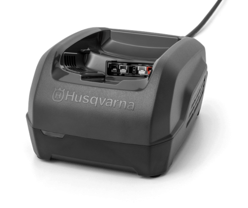 Czarna ładowarka QC250 do akumulatorów Husqvarna, prostokątna, widok z boku. Otwarta z miejscem na akumulator i tylnym wlotem powietrza na jednolitym tle.