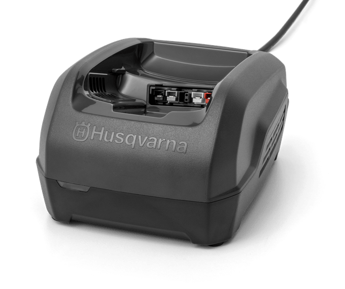 Czarna ładowarka QC250 do akumulatorów Husqvarna, prostokątna, widok z boku. Otwarta z miejscem na akumulator i tylnym wlotem powietrza na jednolitym tle.