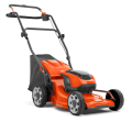 Akumulatorowa kosiarka LC 137i Husqvarna w intensywnym pomarańczowym kolorze, z czarnym koszem na trawę. Produkt w pozycji stojącej, ukazany z boku z detalami rączki i widocznymi dużymi kołami, gotowy do użytku na trawniku.