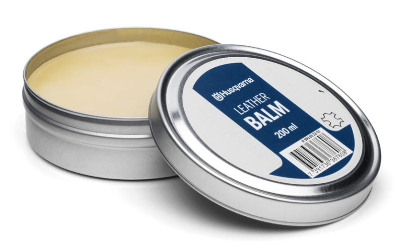 Pasta do butów Husqvarna 200 ml w okrągłym, metalowym opakowaniu. Nakrętka z białą etykietą, na której widnieje napis LEATHER BALM na niebieskim tle. Pozycja produktu: otwarta, widoczne jasnożółte wnętrze kremu.