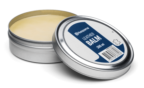Pasta do butów Husqvarna 200 ml w okrągłym, metalowym opakowaniu. Nakrętka z białą etykietą, na której widnieje napis LEATHER BALM na niebieskim tle. Pozycja produktu: otwarta, widoczne jasnożółte wnętrze kremu.