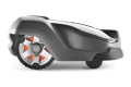 Automower® 430X Husqvarna robot koszący, szary z pomarańczowymi detalami. Widok boczny pokazuje kształt, logo, koła z trójkątnymi wkładkami oraz osłonę ochronną i elementy obrotowe.