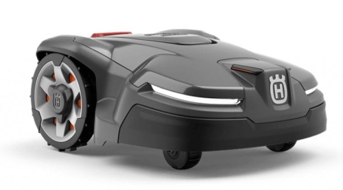 Robot koszący Automower® 405X Husqvarna, w kolorze szarym, z charakterystycznym logo Husqvarna z przodu. Zbliżenie na produkt, nośniki kół widoczne z boku. Wyposażony w diody LED i opływowy kształt, idealny do koszenia trawnika.