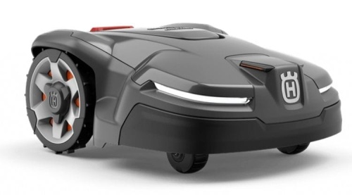 Automower® 415X to robot koszący w kolorze szaro-czarnym z napisem Husqvarna. Ujęcie z przodu, ukazujące aerodynamiczny kształt, widoczne osłony kół i reflektory LED. Produkt stoi na gładkiej powierzchni.