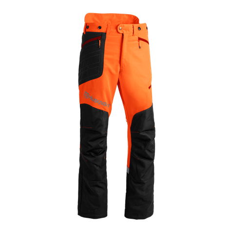 Spodnie do wykaszania Technical Husqvarna w kolorze pomarańczowym i czarnym, z bocznymi kieszeniami, widocznymi wzmocnieniami na kolanach. Ułożone w pozycji stojącej, z detalami szwów i logo na przodzie. Tło w białym kolorze.