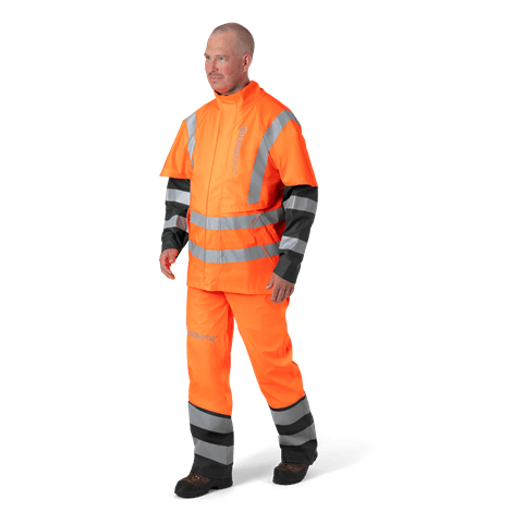Kurtka przeciwdeszczowa Protect High-Viz w intensywnym pomarańczowym kolorze z szarymi odblaskowymi pasami, zapinana na zamek, z krótkim rękawem. Ujęcie frontalne modela stojącego w wodoodpornym ubraniu, widoczne logo Husqvarna. Spodnie w komplecie.