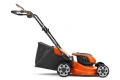 Akumulatorowa kosiarka LC 137i Husqvarna w kolorze pomarańczowym z czarnymi elementami. Ujęcie z boku, kosiarka stoi na czterech kołach. Widoczny pojemnik na trawę z czarnej tkaniny. Wyraźne logo Husqvarna i oznaczenie modelu na obudowie.