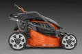 Akumulatorowa kosiarka LC 137i Husqvarna w kolorze pomarańczowym, widoczna z boku, w pozycji leżącej. Posiada duże, szare koła i regulowane uchwyty, z jasno widocznym logo. Tło ciemne, co podkreśla szczegóły produktu.