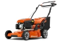 Kosiarka spalinowa Husqvarna LC 353V w kolorze pomarańczowym z czarnymi elementami. Ujęcie frontalne, produkt stoi na podłożu. Wysoka jakość konstrukcji, widoczny napęd silnika oraz rączki do prowadzenia. W zestawie worek na trawę.