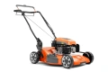 Kosiarka spalinowa LB 256SP Husqvarna w kolorze pomarańczowym z szarymi detalami, widoczna z boku, w pozycji stojącej. Widać silnik, rączkę do prowadzenia oraz duże koła. Na obudowie znajdują się oznaczenia i logo Husqvarna.