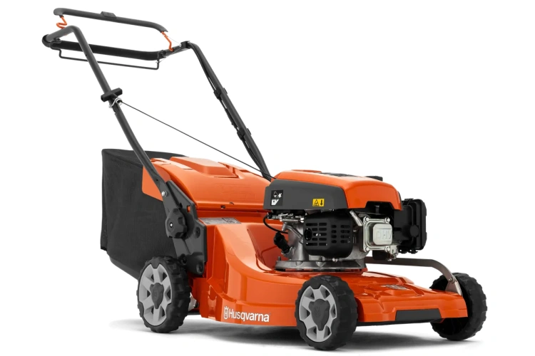 Kosiarka spalinowa Husqvarna LC 247S, pomarańczowy silnik, duże szare koła, ciemny kosz na trawę, logo Husqvarna, aerodynamiczny korpus, widok z boku na płaskiej powierzchni.