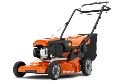 Pomarańczowa kosiarka Husqvarna LC 247S z widocznym metalowym silnikiem, czarnymi kółkami, ergonomicznymi rączkami, osłoną silnika, zbiornikiem paliwa, logo i ostrzeżeniami na obudowie.