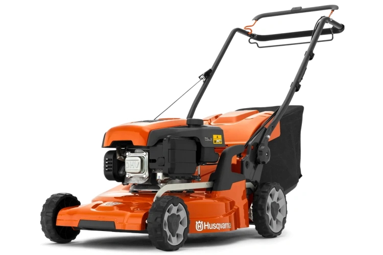 Pomarańczowa kosiarka Husqvarna LC 247S z widocznym metalowym silnikiem, czarnymi kółkami, ergonomicznymi rączkami, osłoną silnika, zbiornikiem paliwa, logo i ostrzeżeniami na obudowie.