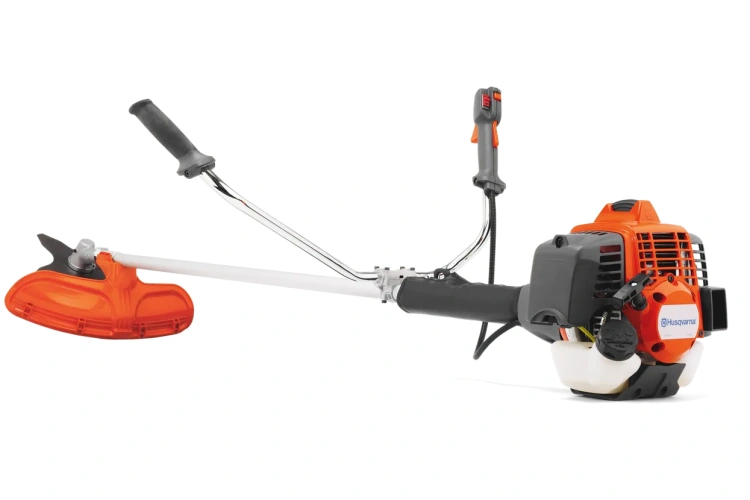 Wykaszarka Husqvarna 553RS w pomarańczowej i szarej kolorystyce z ergonomiczną rączką. Ujęcie boczne, stojąca w pozycji roboczej. Widoczny silnik spalinowy oraz głowica tnąca. Tło białe, co podkreśla szczegóły konstrukcyjne.