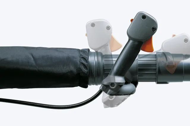Zbliżenie na uchwyt dmuchawy Husqvarna 580BTS z ergonomiczną rączką. Widoczne elementy sterujące oraz zewnętrzna osłona w ciemnym kolorze. Kąt ujęcia pokazuje detale mocowania i fakturę materiału. Tło jednolite, neutralne.