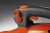 Zbliżenie na uchwyt dmuchawy Husqvarna 580BTS, w kolorze pomarańczowym i czarnym. Widoczne przyciski, w tym czerwony włącznik oraz regulacja mocy. Uchwyt ma ergonomiczną teksturę, co ułatwia trzymanie. Tło jest jednolite, ciemne.