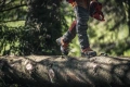 Buty skórzane Technical 24 Husqvarna w kolorze brązowym, z widocznymi pomarańczowymi akcentami. Ujęcie z boku, na tle drewnianego pnia. Buty mają wyraźny, teksturowany materiał, solidną podeszwę i są w użyciu podczas spaceru w terenie.