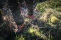 Pomarańczowe buty skórzane Technical 24 Husqvarna z czarnymi detalami i ochraniaczami przed przecięciem, stojące na błotnistym podłożu z zieloną trawą, ukazujące funkcjonalność w trudnych warunkach.