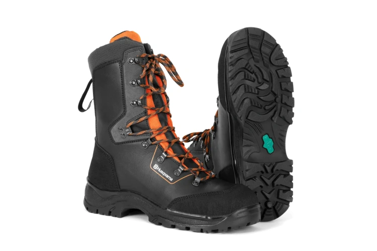 Buty z ochroną przed przecięciem Classic Husqvarna w kolorze czarnym z pomarańczowymi sznurówkami. Ujęcie z boku, ukazujące podeszwę z wyraźnym bieżnikiem oraz detalowe mocowanie sznurówek. Wykonane z materiałów odpornych na uszkodzenia.