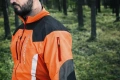 Kurtka do prac leśnych Technical Arbor Husqvarna w intensywnym pomarańczowym kolorze, z czarnymi wstawkami i charakterystycznym logo. Z przodu widoczny zamek oraz kieszeń na rękawie. Produkt noszony na modelu, w naturalnym otoczeniu leśnym.