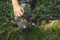 Nogawki ochronne Classic Husqvarna w kolorze szarym, wykonane z wytrzymałego materiału, zasuwane na zamek. Produkt umieszczony w terenie leśnym, częściowo założony na but, z widoczną jedynie górną częścią nogawek.