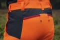 Spodnie ochronne Technical High Viz Husqvarna w kolorze pomarańczowym z czarnymi detalami. Boki z zamkami zasuwanymi, widoczny pas i wszywki. Ujęcie z tyłu, ukazujące detale oraz strukturę materiału.