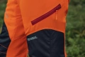 Spodnie ochronne Technical High Viz Husqvarna w intensywnym pomarańczowym kolorze z czarnymi elementami. Widoczny zamek błyskawiczny przy kieszeni oraz haftowane logo TECHNICAL. Kąt ujęcia z boku, ukazujący detal materiału i konstrukcji.