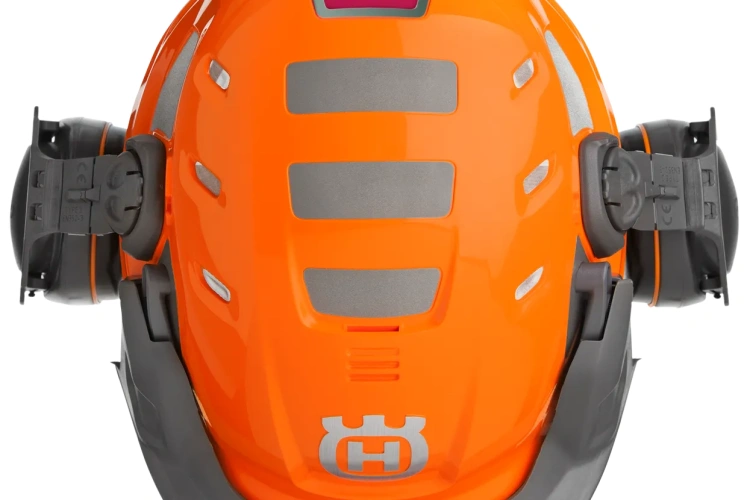 Kask leśny Technical Husqvarna w kolorze pomarańczowym, widok z tyłu. Wyróżniają się szare elementy wentylacyjne oraz logo w dolnej części. Kask ma regulowane mocowania z boku, zapewniające stabilne dopasowanie. Tło proste, jednolite.