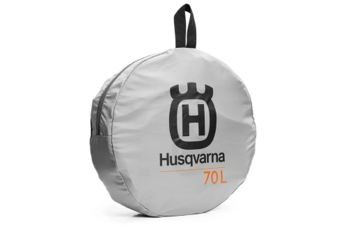 Torba podróżna Husqvarna Xplorer w kolorze szarym, zapinana na zamek. Okrągły kształt, z logo Husqvarna i pojemnością 70 litrów. Ujęcie z boku, leżąca na płaskiej powierzchni, pokazująca materiał i detale wykończenia.