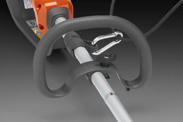 Podkrzesywarka akumulatorowa Husqvarna 530iP4 z uchwytem w kształcie półokręgu, metalowym uchwytem i oświetleniem wskaźnika mocy. Rura aluminiowa z oznaczeniem, zamontowany karabińczyk do mocowania. Tło w odcieniu ciemno-szarym.