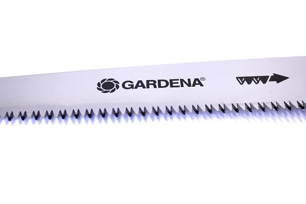Piła ogrodowa GARDENA 300P z metalowym ostrzem i ząbkami, widoczna z boku. Na ostrzu widoczna jest czytelna nazwa marki GARDENA oraz strzałka wskazująca kierunek cięcia. Ostrze ma matowe wykończenie, a ząbki są ostre.