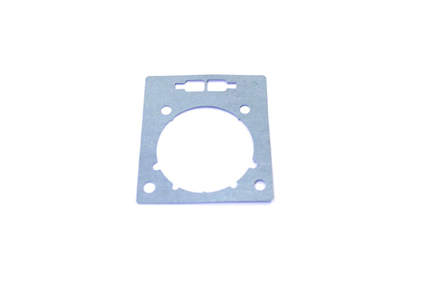 Uszczelka cylindra do kosy Husqvarna 535RX/135R/535RXT/336FR. Metalowa, płaska, w kształcie prostokąta z wycięciem na środkowym okręgu oraz czterema otworami montażowymi. Widok frontalny na białym tle.