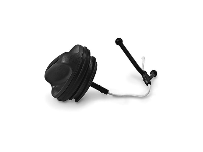 Czarny korek oleju do pilarki Husqvarna 543XP/543XPG, okrągły z teksturowaną powierzchnią i białą elastyczną linką. Leży płasko, widoczne dwa zaczepy do mocowania, służy do zabezpieczenia oleju.