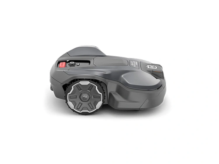 Robot koszący Husqvarna Automower®320 NERA w kolorze ciemnoszarym, widok z boku. Posiada dwa dużymi, metalowymi kołami z wyraźnym wzorem. W górnej części znajdują się przyciski oraz logo Husqvarna. Produkt leży na białym tle.