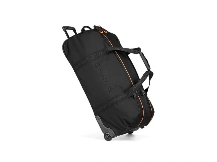 Torba turystyczna Xplorer 90L Husqvarna w kolorze czarnym, z pomarańczowymi detalami. Stojąca, z wysuwanym uchwytem i kółkami, zamknięta na zamek błyskawiczny. Charakteryzuje się logo Husqvarna na boku i krótkimi uchwytami do przenoszenia.