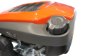 Silnik HS 166AE do kosiarki Husqvarna, widok z boku, z detalem korka wlewu paliwa. Obudowa w kolorze pomarańczowym z szarym wykończeniem. Widoczne elementy montażowe oraz wentylacja na górze. Kształt zaokrąglony, ergonomiczny.
