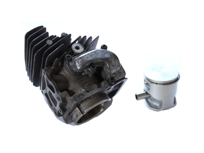 Cylinder kompletny pilarki Husqvarna 550XP/550XPG w kolorze szarym z metaliczną fakturą. Widok z boku ukazuje żebrowaną strukturę. Obok znajduje się tłok z chromowanym wykończeniem. Produkty leżą na białym tle.