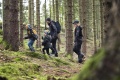 Kurtka męska Husqvarna Xplorer Shell na modelu w ciemnym otoczeniu leśnym. Widoczne elementy: czarna kolorystyka, funkcjonalny krój, logo na rękawie, zamek błyskawiczny z przodu, kieszenie. Produkt używany w terenie, w towarzystwie rodziny.