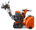 Pomarańczowa odśnieżarka ST 427T Husqvarna z dużym wirnikiem, metalowym podwoziem, gumowymi gąsienicami, ergonomicznymi uchwytami i panelem sterującym. Prosta i łatwa w obsłudze.
