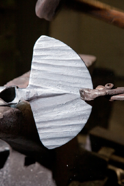 Motyczka ogrodowa 2-stronna w kształcie serca i prostokąta, stylisko o długości 40 cm. Zbliżenie na metalową głowicę z delikatnym, teksturowanym wykończeniem. Narzędzie leży poziomo na blacie, na tle ciemnej powierzchni.