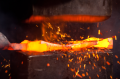 Proces kowalstwa: na czarnym kowadle gorący, emitujący pomarańczowo-czerwone światło metal, iskry wokół. Ręka kowala trzyma narzędzie, formując materiał na tle podkreślającym blask ognia.
