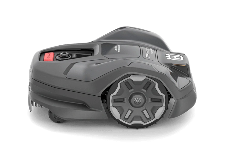 Robot koszący Husqvarna Automower® 310E NERA, w kolorze szarym, z zaokrąglonym kształtem i eleganckimi, kontrastowymi detalami. Ujęcie z boku, ukazujące położenie montażowe z widocznym przyciskiem start. Idealny do ogrodu, łatwy w obsłudze.
