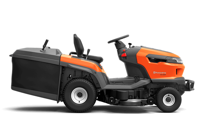 Traktor TC 220T Husqvarna w kolorze pomarańczowym i czarnym, widoczny z boku, z zainstalowanym koszem na trawę. Siedzenie z wysokim oparciem, kierownica z kontrolkami. Opony terenowe, solidna konstrukcja, przystosowany do pracy w ogrodzie.