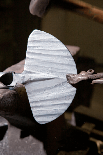 Motyka sercowa z jesionowym styliskiem o długości 130 cm. Widok z boku na metalowy, lekko teksturowany ostrze, mocowane do rączki. Tło ciemne, co podkreśla detal wykonania narzędzia.