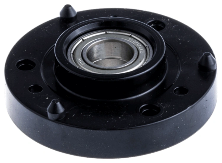 Obudowa łożyska do Automower 310/405X Husqvarna w kolorze czarnym, o okrągłym kształcie. Widoczny metalowy element łożyska oraz sześć otworów mocujących wokół. Produkt leży na płaskiej powierzchni, z bliska, ukazując detal konstrukcji.
